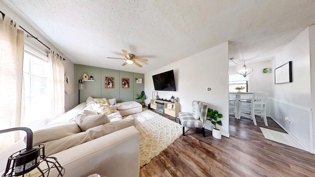 living room with dark hardwood / wood-style floors, ceiling fan with notable chandelier, and a textured ceiling