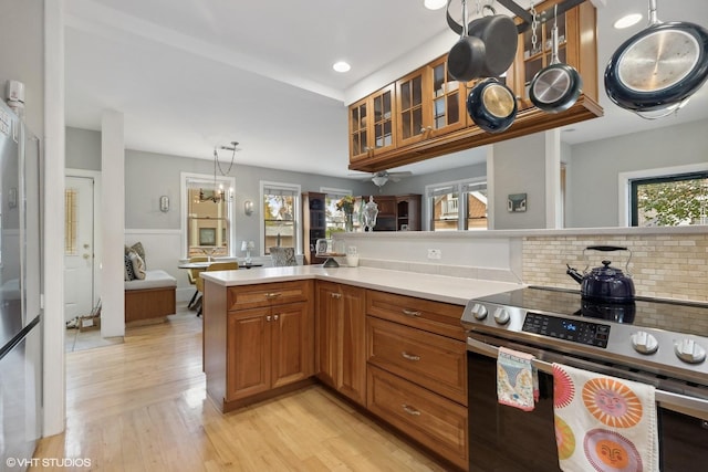 kitchen with pendant lighting, stainless steel range with electric stovetop, backsplash, light hardwood / wood-style floors, and kitchen peninsula