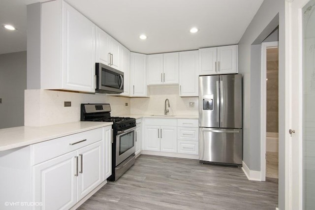 kitchen with sink, white cabinetry, light wood-type flooring, stainless steel appliances, and decorative backsplash