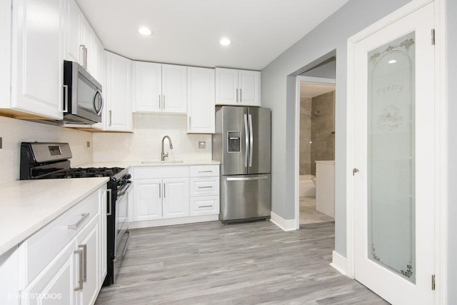 kitchen featuring sink, light hardwood / wood-style flooring, stainless steel appliances, tasteful backsplash, and white cabinets