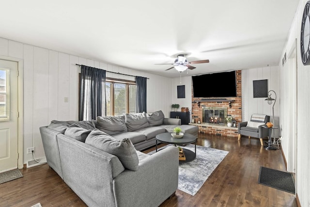 living room with a brick fireplace, dark wood-type flooring, and ceiling fan