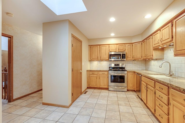 kitchen featuring sink, light stone counters, a skylight, light brown cabinets, and appliances with stainless steel finishes