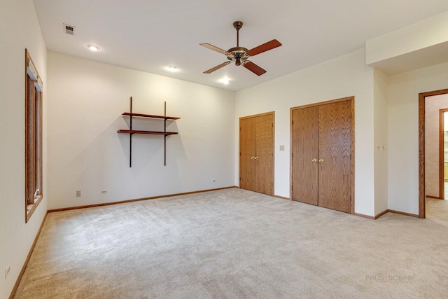 unfurnished bedroom with two closets, light colored carpet, and ceiling fan