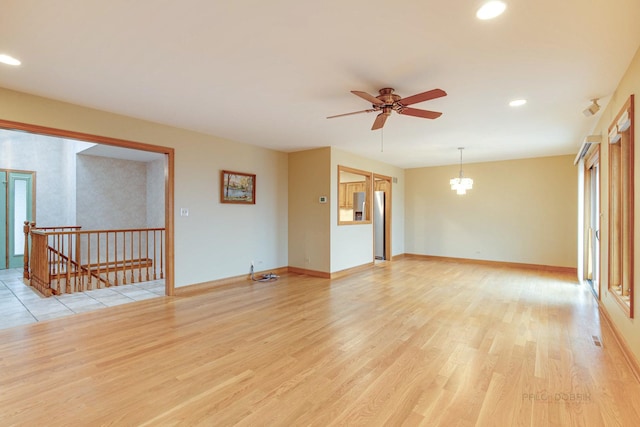 spare room with ceiling fan with notable chandelier and light hardwood / wood-style floors