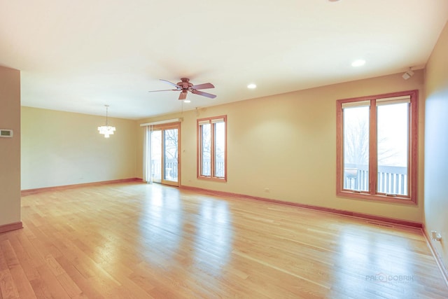 empty room featuring ceiling fan with notable chandelier and light hardwood / wood-style floors