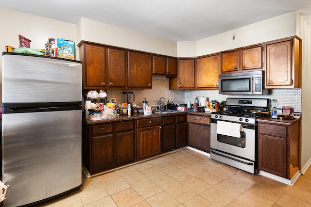 kitchen featuring sink, light tile patterned floors, dark stone counters, stainless steel appliances, and decorative backsplash