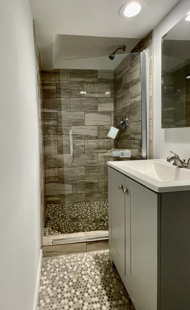 full bath with baseboards, tiled shower, and vanity