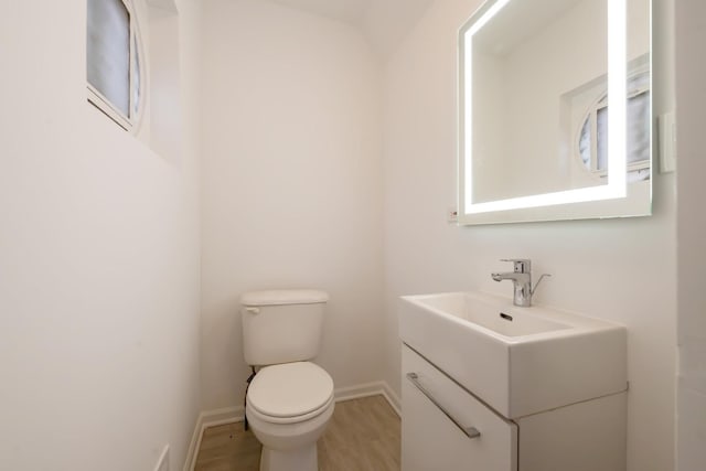 half bath with vanity, wood finished floors, toilet, and baseboards