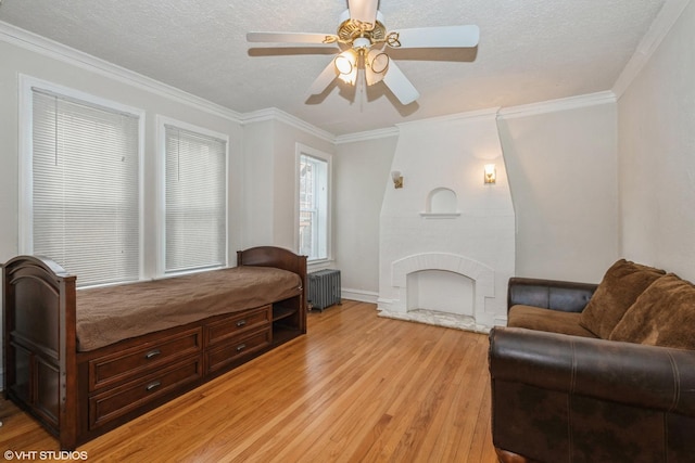 bedroom with crown molding, a brick fireplace, a textured ceiling, radiator heating unit, and light hardwood / wood-style floors