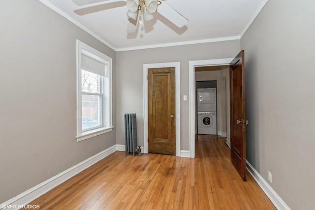 unfurnished bedroom with stacked washing maching and dryer, radiator heating unit, ceiling fan, crown molding, and light hardwood / wood-style flooring