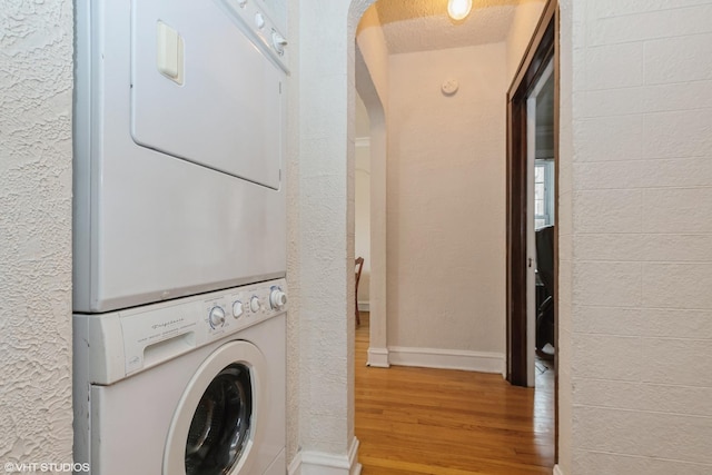 washroom featuring stacked washer and dryer, light hardwood / wood-style flooring, and a textured ceiling