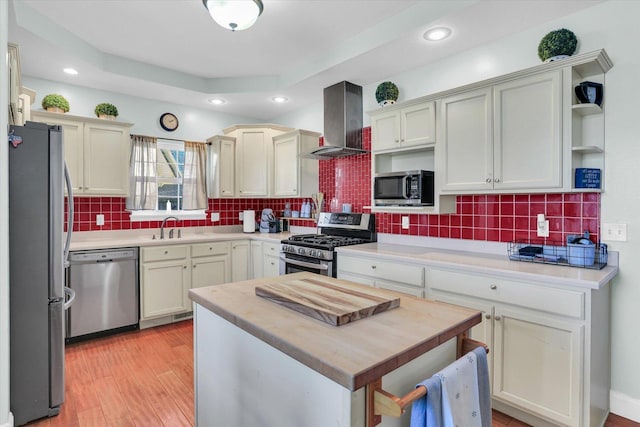 kitchen with sink, appliances with stainless steel finishes, light hardwood / wood-style floors, decorative backsplash, and wall chimney range hood