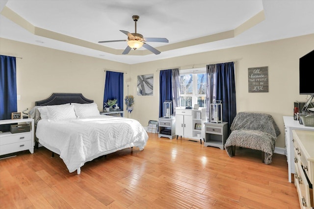 bedroom with a raised ceiling, ceiling fan, and light wood-type flooring