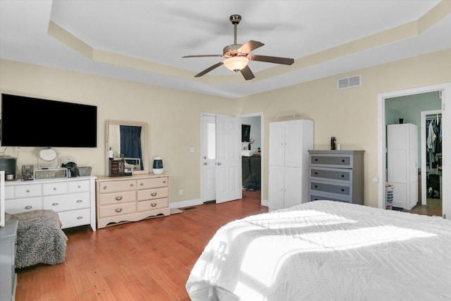 bedroom featuring hardwood / wood-style flooring, a walk in closet, ceiling fan, a raised ceiling, and a closet