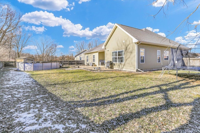 rear view of house with a fenced in pool, a trampoline, and a lawn