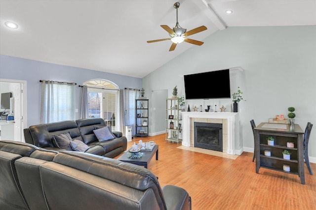 living room with high vaulted ceiling, beamed ceiling, a tiled fireplace, ceiling fan, and light hardwood / wood-style floors