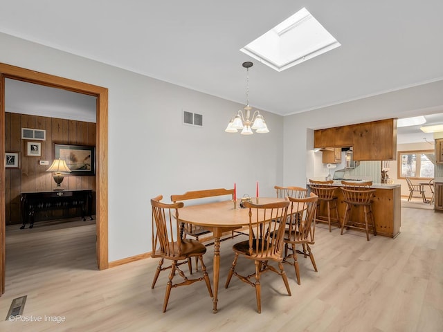 dining area featuring wood walls, an inviting chandelier, a skylight, light hardwood / wood-style flooring, and ornamental molding