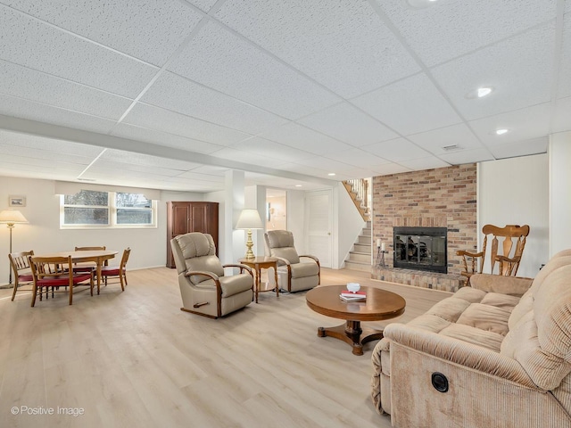 living room featuring a paneled ceiling, a fireplace, and light wood-type flooring