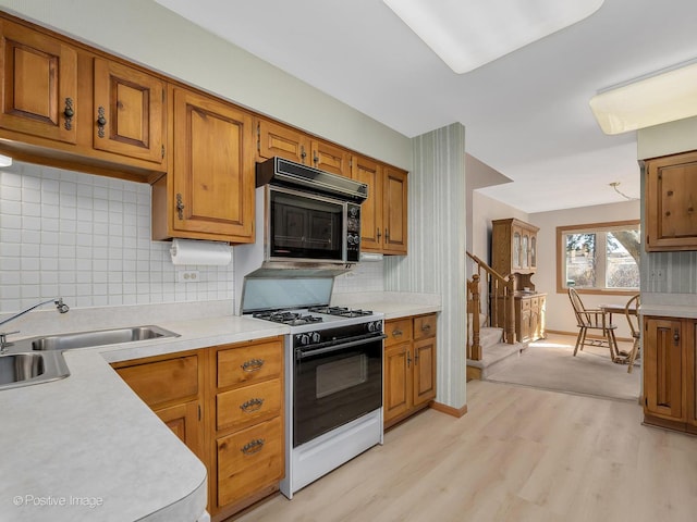 kitchen featuring backsplash, range with gas stovetop, sink, and light wood-type flooring