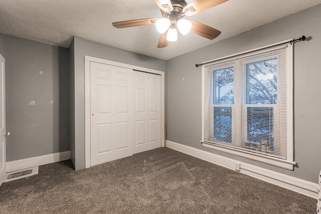 unfurnished bedroom featuring ceiling fan, a textured ceiling, dark carpet, and a closet