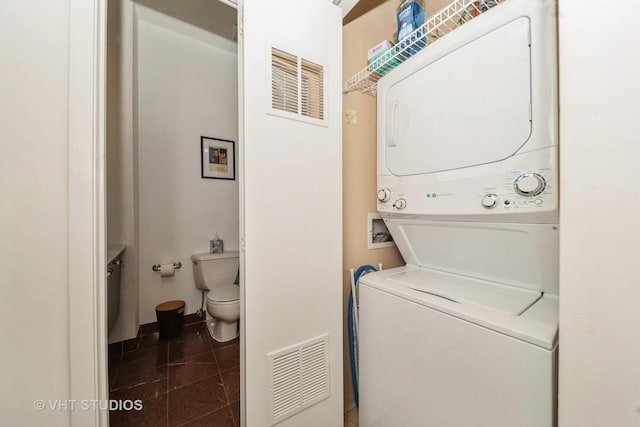 washroom with stacked washer and clothes dryer and dark tile patterned floors