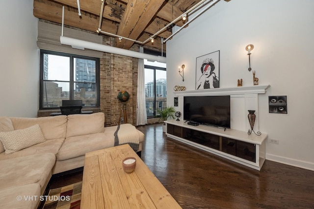 living room with a high ceiling, brick wall, track lighting, and dark hardwood / wood-style flooring