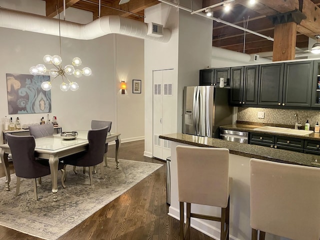 kitchen with a towering ceiling, dark hardwood / wood-style floors, sink, hanging light fixtures, and stainless steel appliances