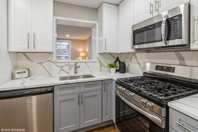 kitchen with stainless steel appliances, light stone countertops, sink, and gray cabinetry