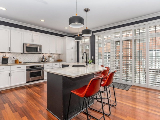 kitchen featuring sink, white cabinetry, a center island with sink, pendant lighting, and stainless steel appliances