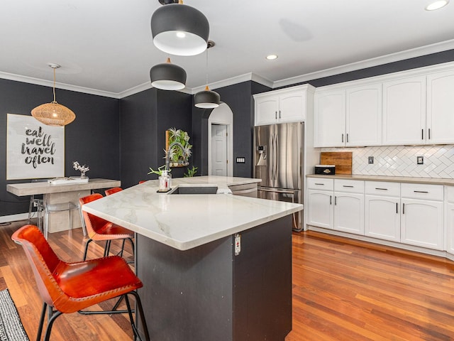 kitchen with an island with sink, sink, pendant lighting, and stainless steel fridge with ice dispenser