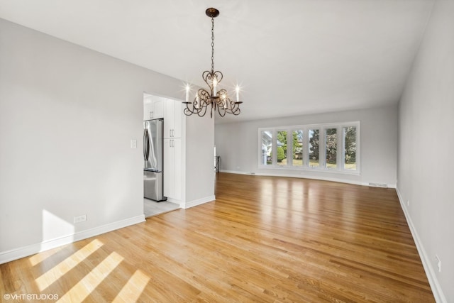 empty room with a chandelier and light hardwood / wood-style flooring