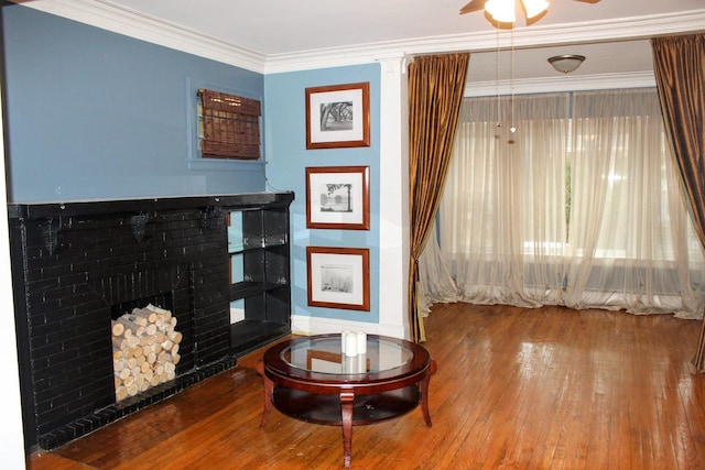 living room featuring ceiling fan, ornamental molding, wood-type flooring, and a brick fireplace