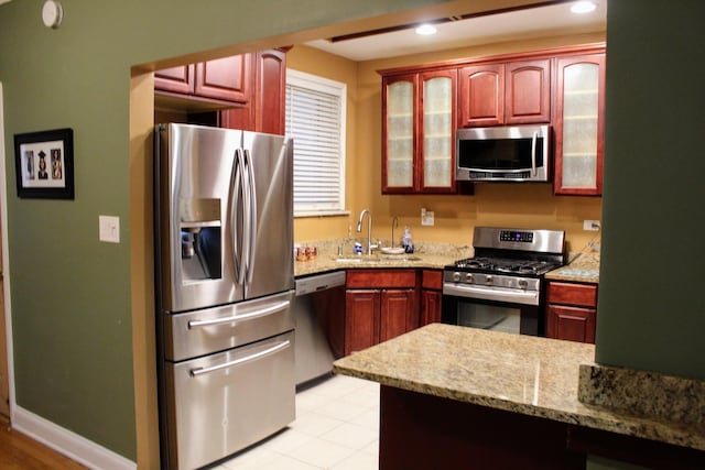 kitchen featuring stainless steel appliances, kitchen peninsula, sink, and light stone countertops