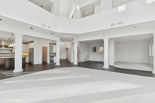 unfurnished living room with sink, a towering ceiling, and decorative columns