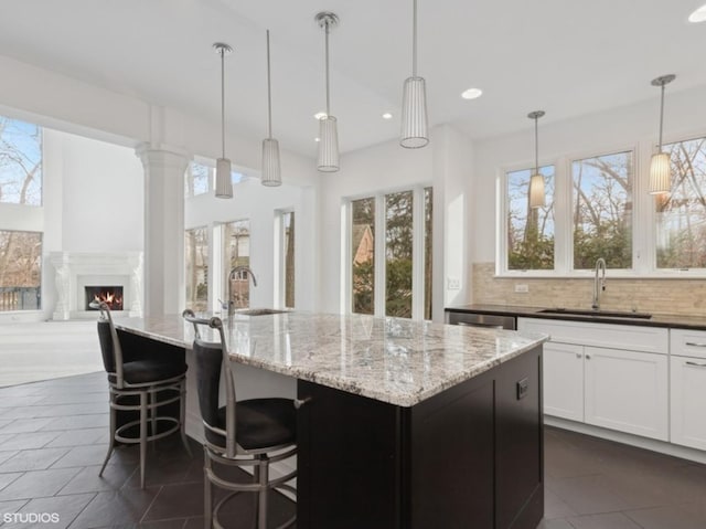 kitchen featuring pendant lighting, a kitchen island with sink, sink, and dark stone countertops