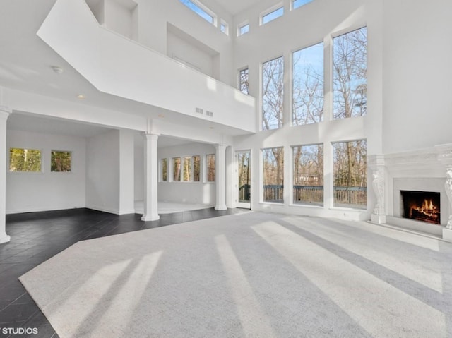 unfurnished living room featuring ornate columns, plenty of natural light, and a high end fireplace