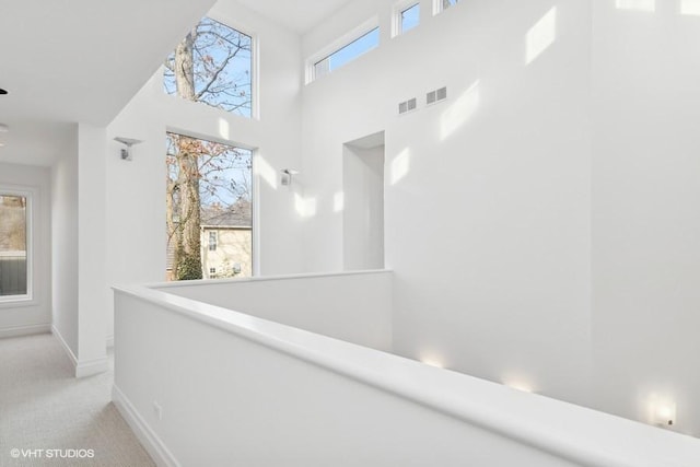 hall featuring a towering ceiling and light colored carpet