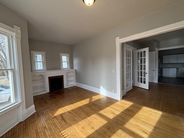 unfurnished living room featuring wood-type flooring, a wealth of natural light, a fireplace, and french doors