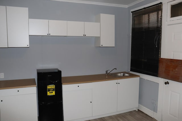 kitchen featuring white cabinetry, sink, crown molding, and light wood-type flooring