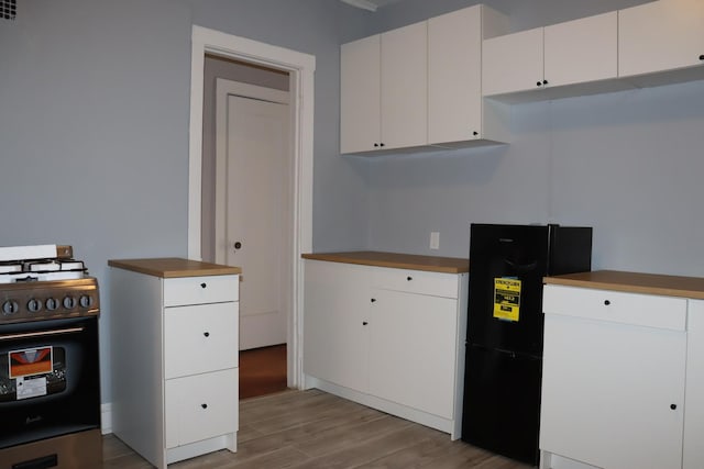 kitchen with white cabinetry, black fridge, gas range oven, and light hardwood / wood-style flooring