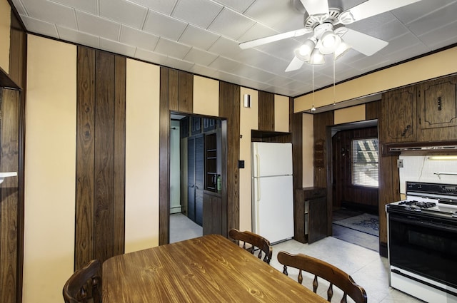 kitchen featuring dark brown cabinetry, wood walls, gas range, white fridge, and a baseboard heating unit