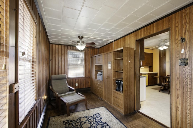 living area with dark parquet flooring, ceiling fan, and wood walls