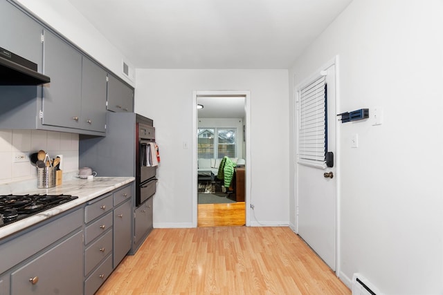 kitchen featuring light hardwood / wood-style flooring, a baseboard radiator, gray cabinets, decorative backsplash, and exhaust hood