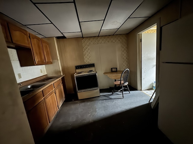 kitchen featuring brown cabinets, freestanding refrigerator, a drop ceiling, and range with electric cooktop