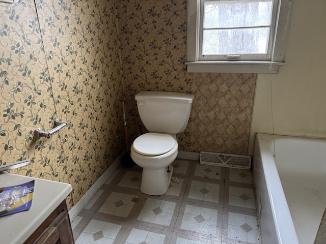 bathroom featuring visible vents, baseboards, toilet, a tub, and wallpapered walls