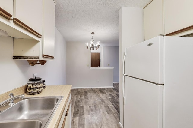 kitchen featuring sink, light hardwood / wood-style flooring, white refrigerator, pendant lighting, and white cabinets