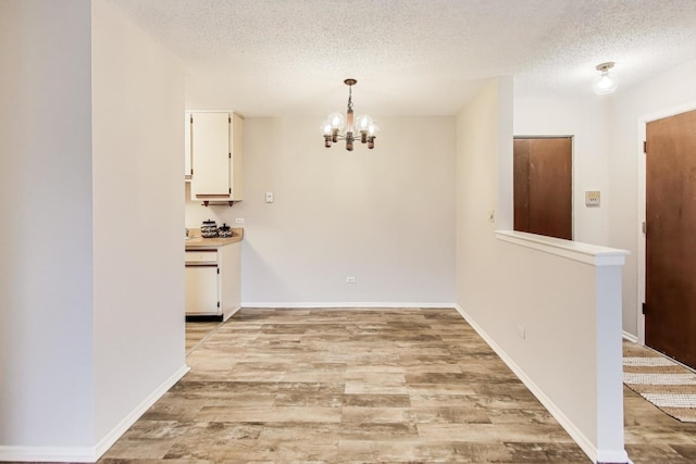 unfurnished dining area featuring light hardwood / wood-style floors, a chandelier, and a textured ceiling