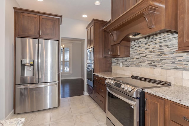 kitchen featuring custom exhaust hood, stainless steel appliances, tasteful backsplash, light stone countertops, and baseboards