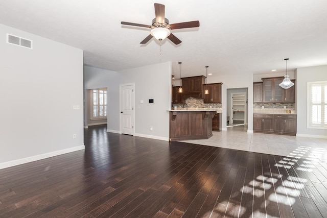 unfurnished living room with light wood-style floors, visible vents, ceiling fan, and baseboards