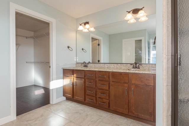 bathroom featuring a spacious closet, double vanity, a sink, and baseboards